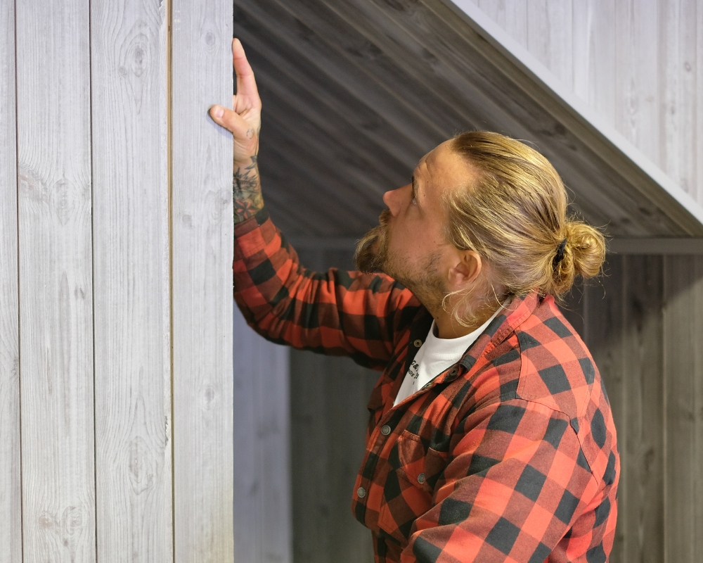 En man med röd- och svartrutig skjorta och en grå träpanel