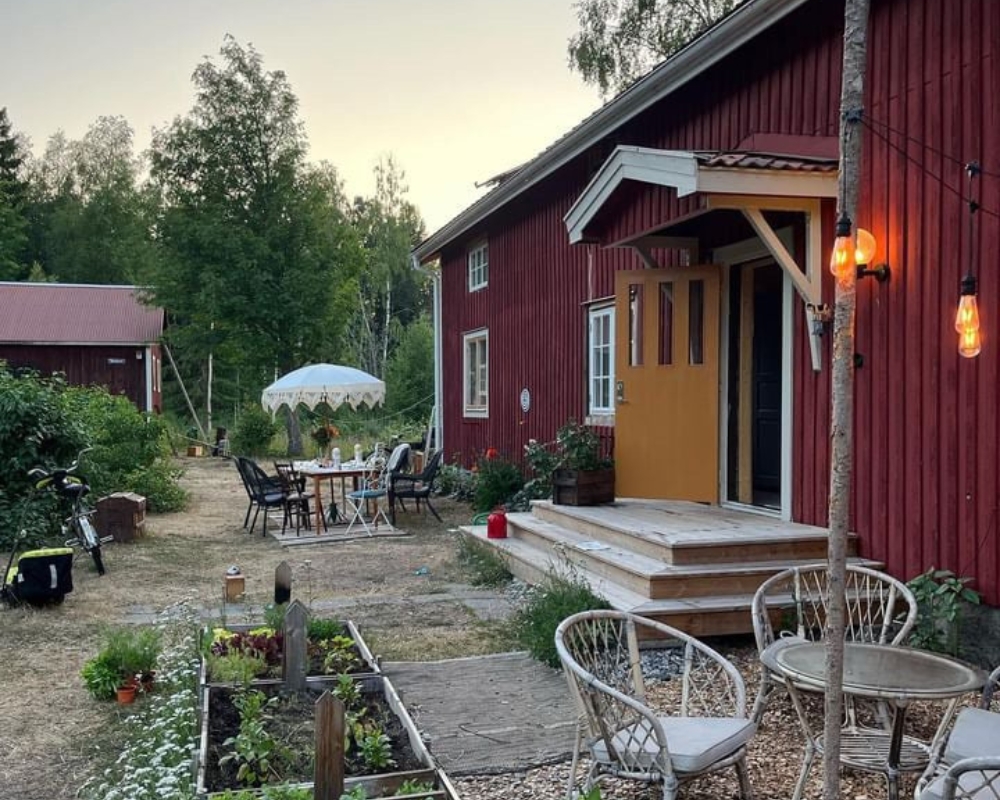 ett rött hus med gul dörr och en trädgård med odlingar och trägårdsmöbler