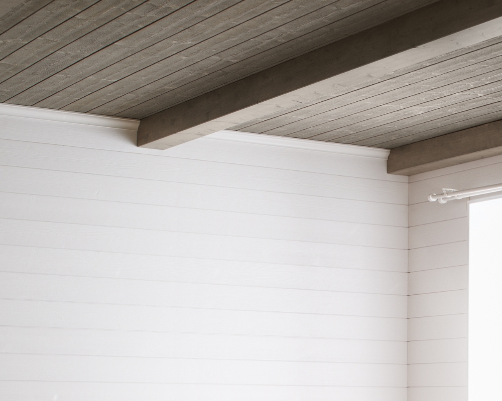 Ett innertak med träpanel och bjälkar, samt en vi träpanel på väggen