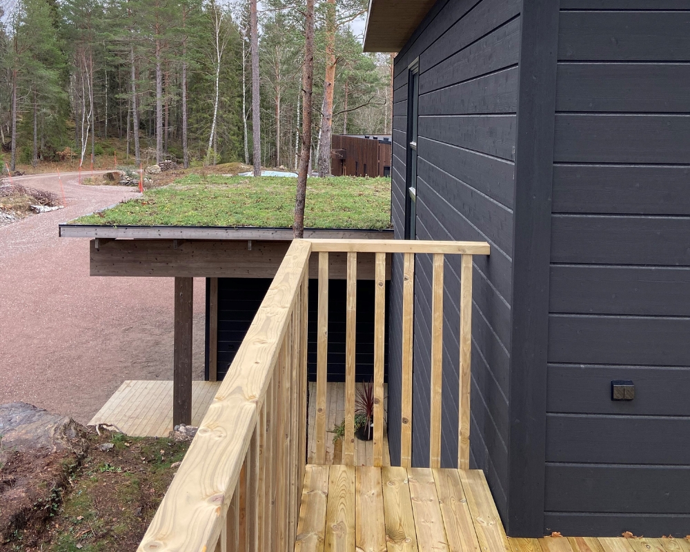 Ett hus med svart limträpanel och en trall