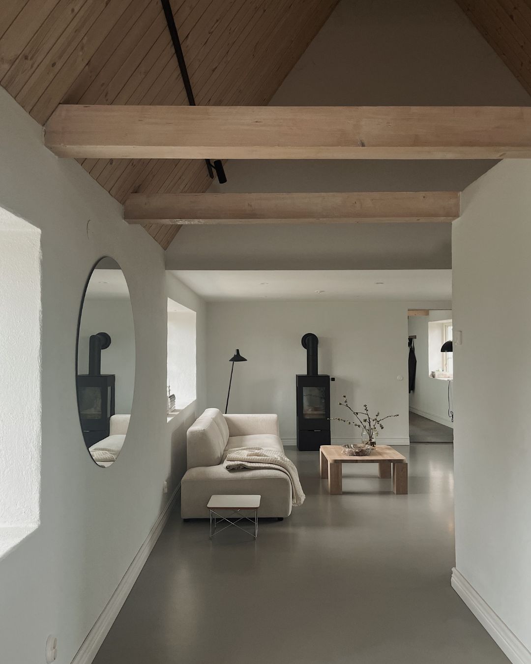 Ljust och minimalistiskt möblerat hem med soffa, bord och en svart kamin,  trätaket går upp i knock