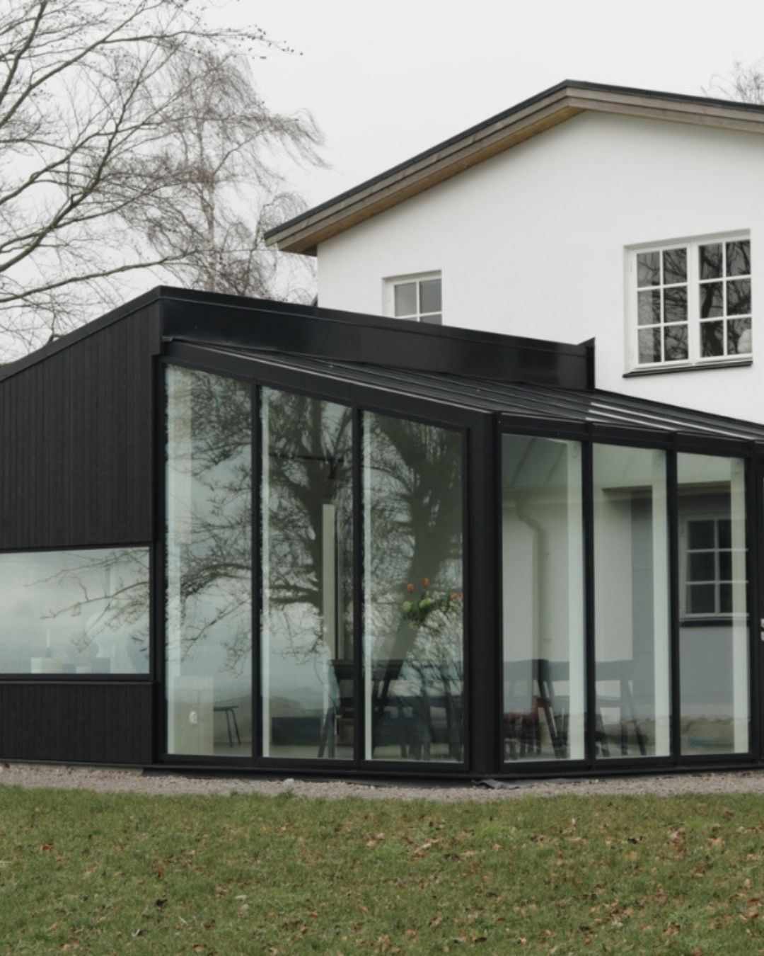 Vitt stenhus med tillbyggnad som är svart med stora glaspartier