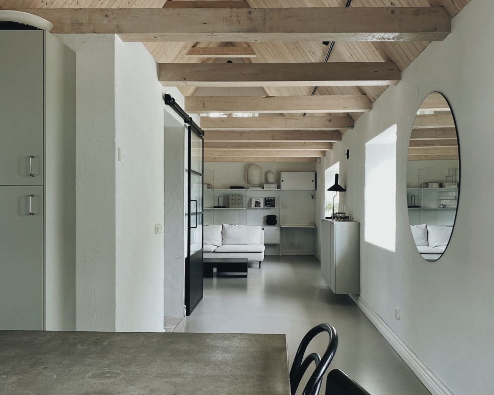 Ett industriellt rum, med bord och stolar, samt ljus soffa och en vit bokhylla