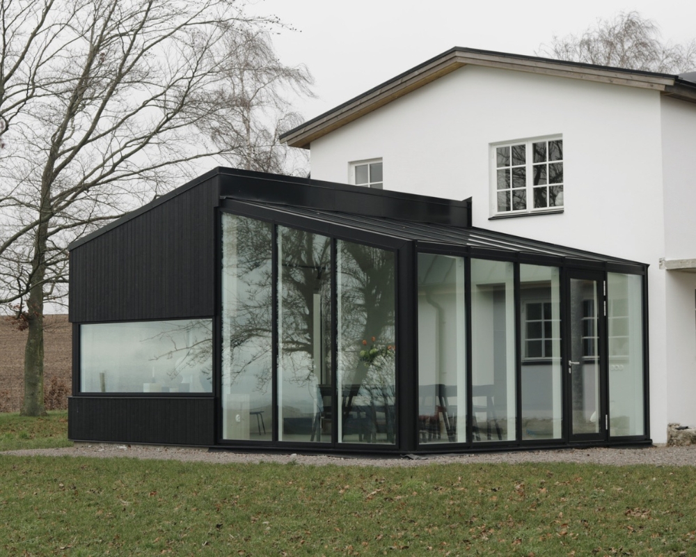 Ett vitt hus med en utbyggnad i form av en inglasning med svart ram