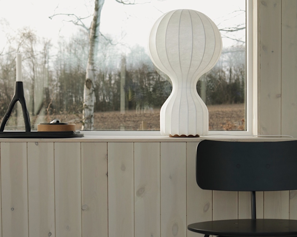 ett fönster med lampa och dekoration, en ljus träpanel och en svart stol