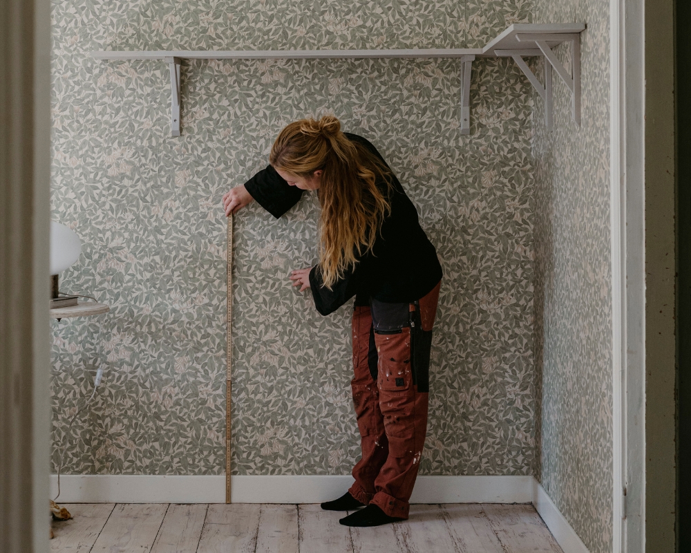 En kvinna mäter med en tumstock från golv upp på vägg