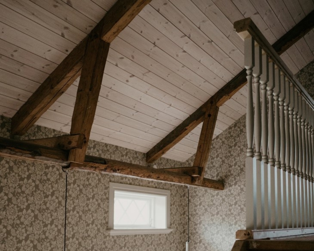 Ett tak med ljus träpanel, samt bruna träbalkar