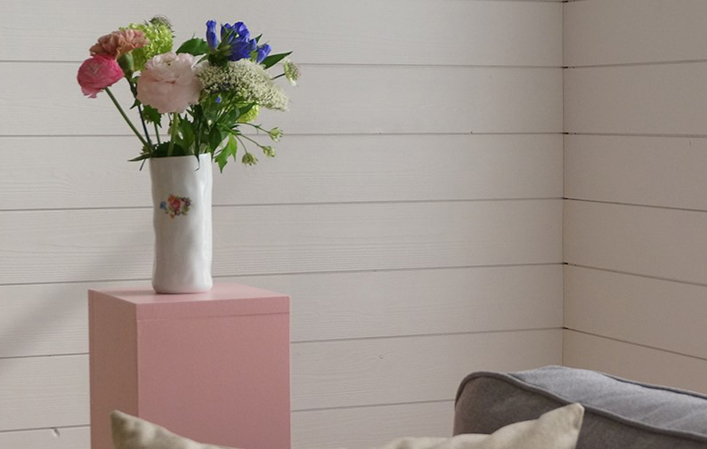 En rosa piedesal med blommor, samt en vit träpanel