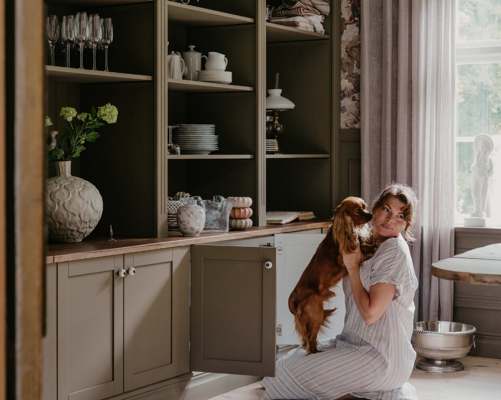 En kvinna sitter på golvet med en hund i sitt knä, framför en platsbyggd bokhylla