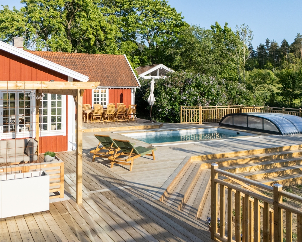 Ett rött hus, altan i trä, pool och utemöbler