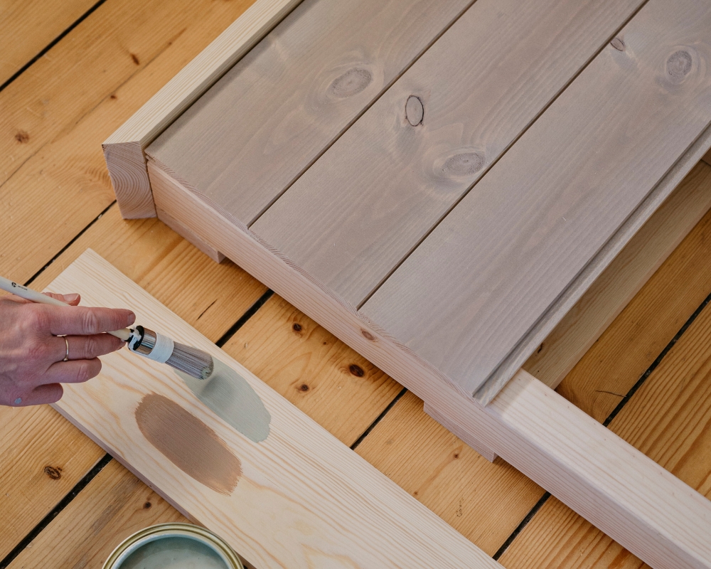 En sänggavel i trä ska målas. Visar två färger på en bräda