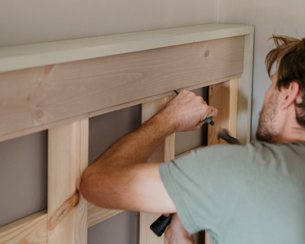 en man monterar en sänggavel i trä mot väggen