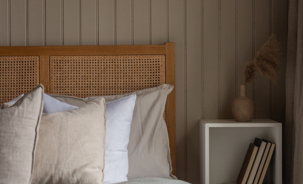 Hörnet på en säng med flera kuddar, ett sängbord med vas och en beige pärlspont träpanel