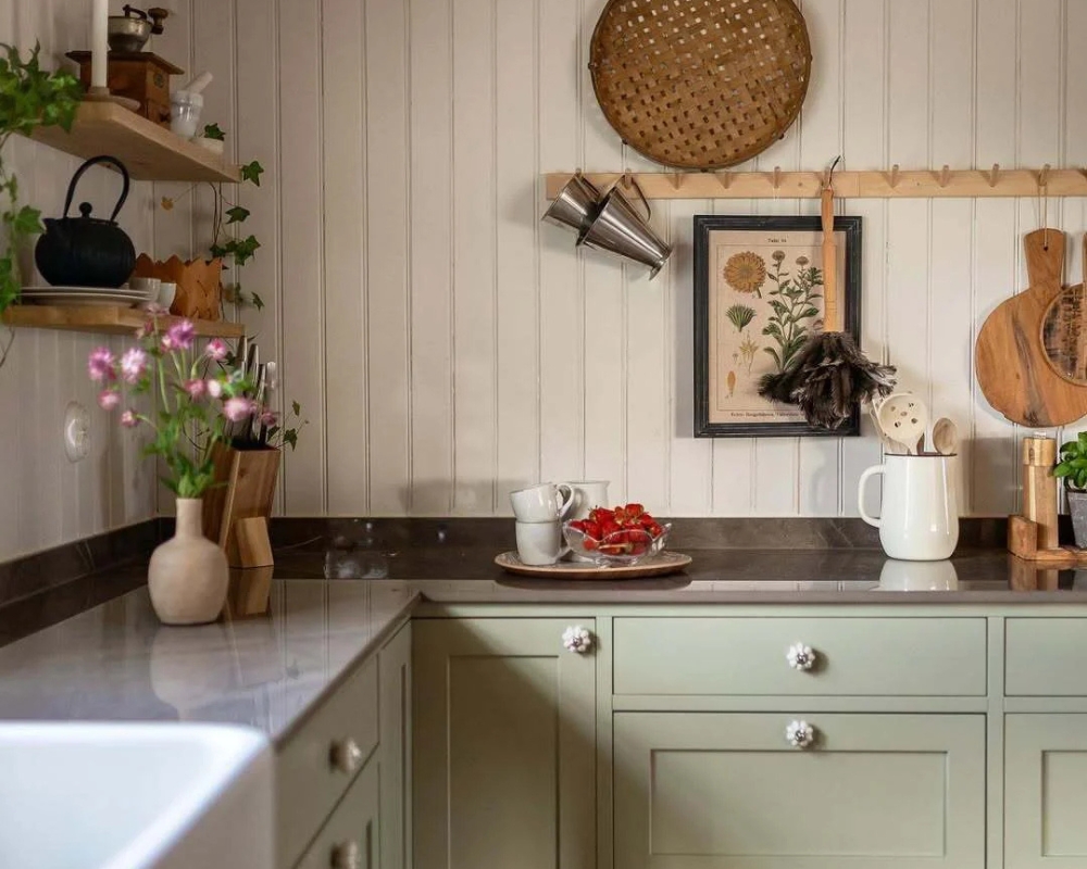 En köksbänk med gröna lådor och en vit pärlspont träpanel, samt dekorationer
