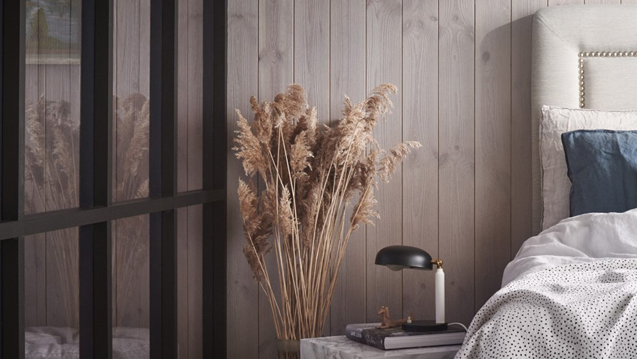 Sovrum med skiljevägg av plexiglas med svarta träreglar, en säng och sängbord med lampa