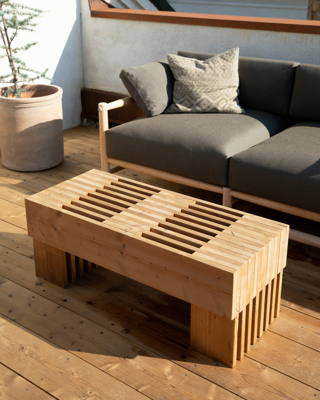 Platsbyggt soffbord av spillvirke i TermoGran på takterrassen, placerat framför en utesoffa med grå dynor.