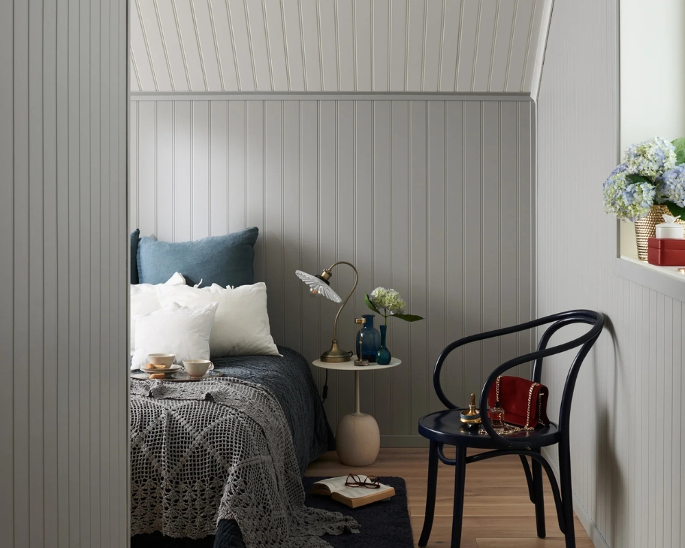 Grå pärlspont träpanel på väggar och tak, trägolv och en säng, samt inredningsdetaljer