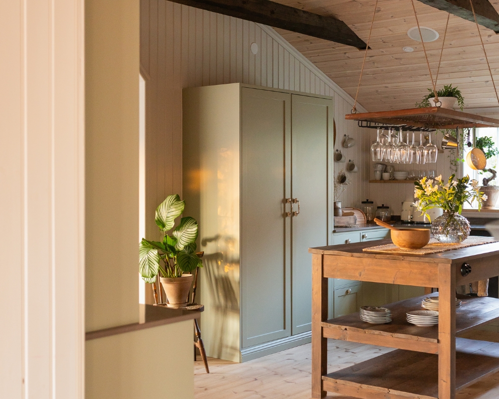 Ett kök med trä från golv till tak. En köksö i trä, ett grönt skåp och inredningsdetaljer