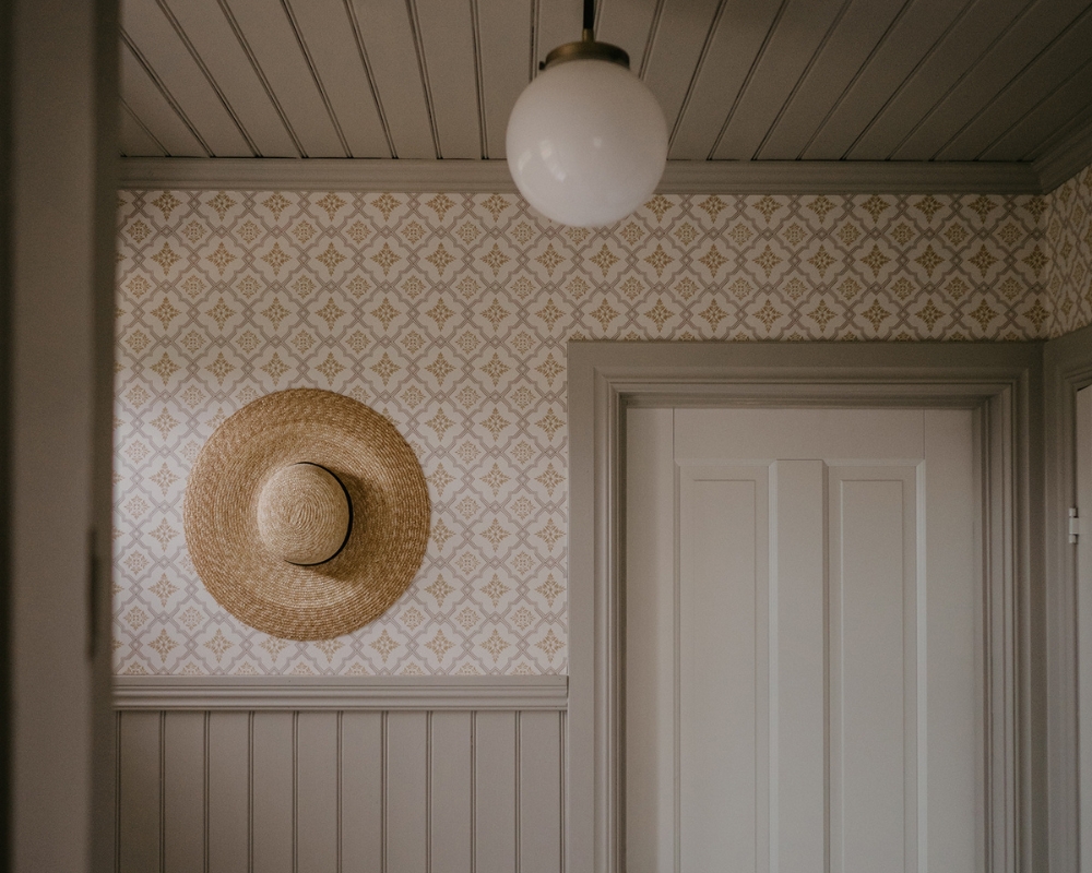 Bröstpanel och tak i träpanelen Pärlspont, tapet med mönster, en lampa i taket och en hatt på väggen