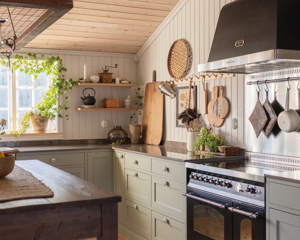 ett kök med träpanel, trägolv, trätak, och en köksbänk med gröna luckor och svart spis, samt en köksö i mörkt trä. Och även dekorationer och köksredskap