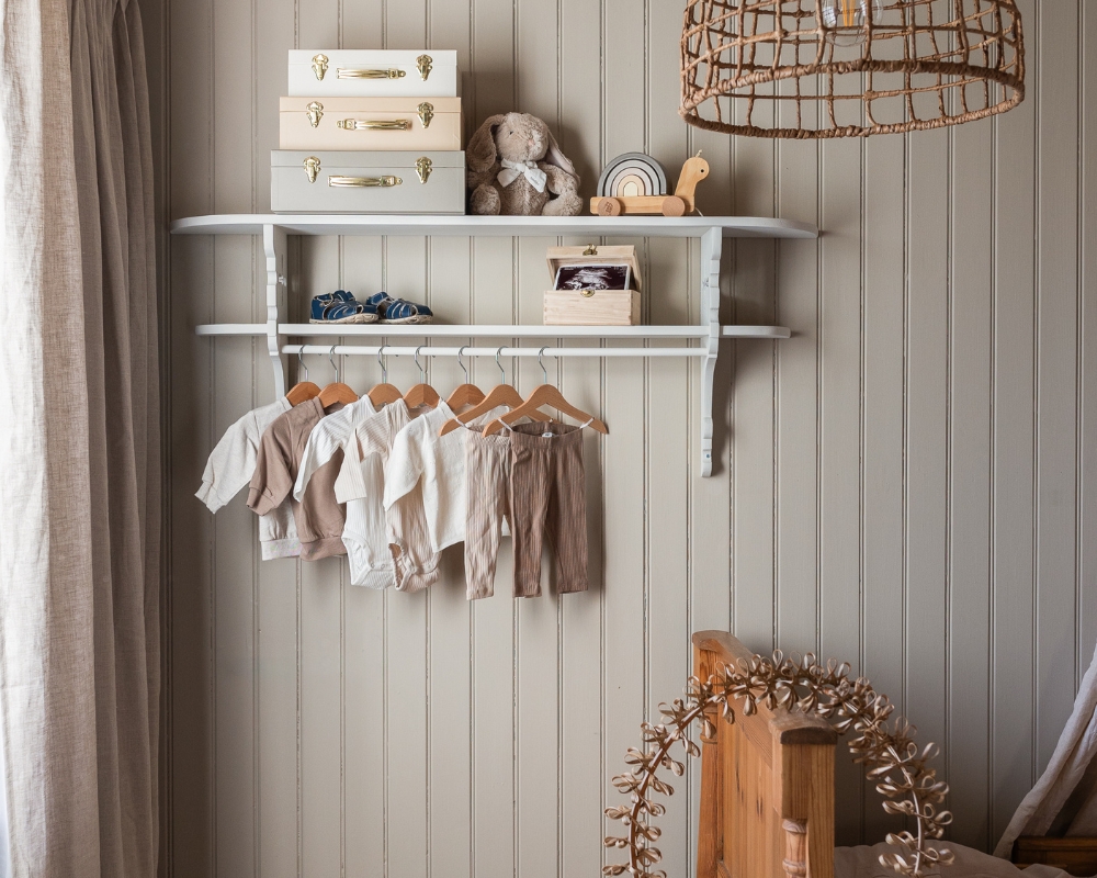 En vit hylla med barnkläder och väskor på en beige träpanel