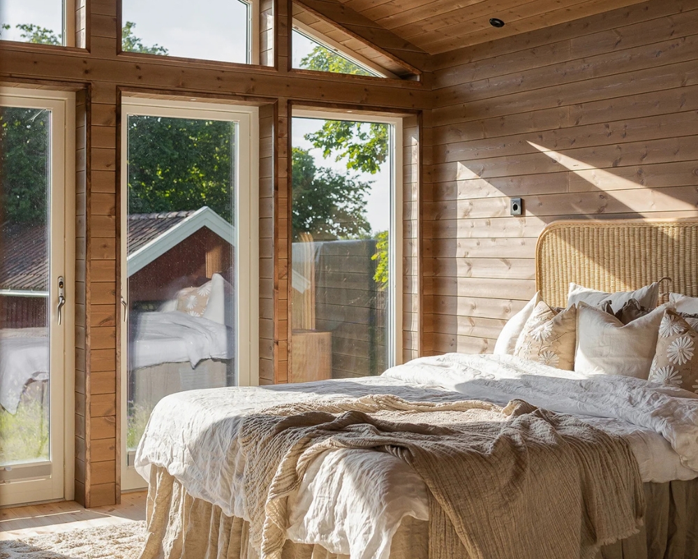 Ett sovrum med höga fönster och träpanel, samt en säng