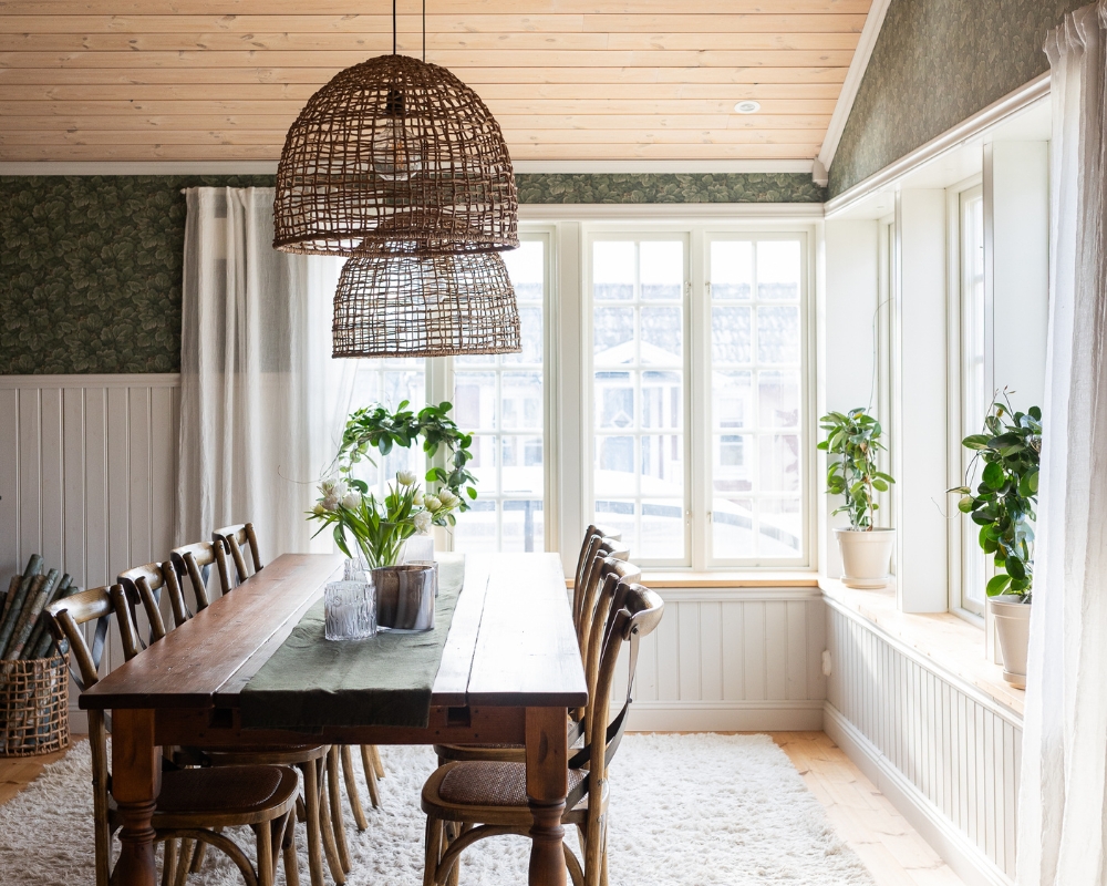 Matsal i ett hem med vit bröstpanel, trätak och trägolv, samt köksbord och stolar, med en stor vit matta