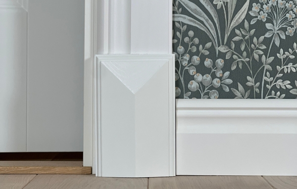 Vit golvkloss och vita lister, samt en grön tapet med mönster