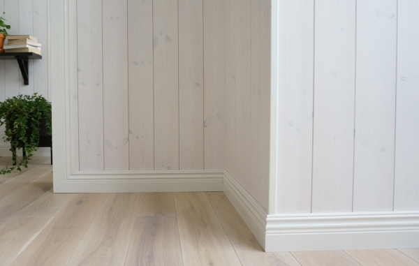 En vägg med vit panel och vita lister, samt ett trägolv