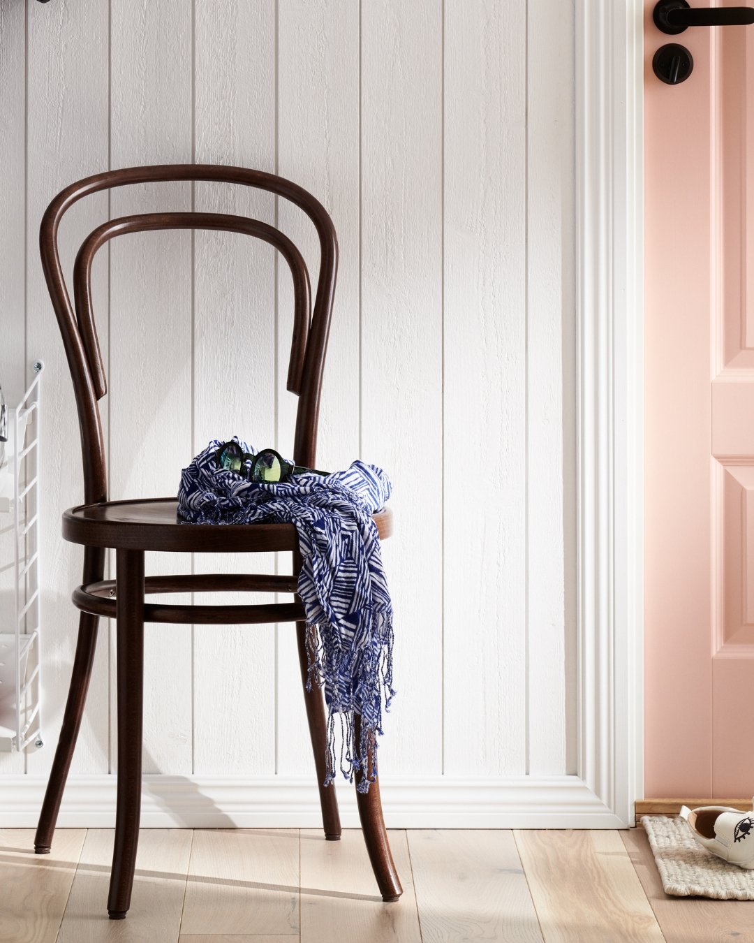 Vit panel och lister, trägolv och en brun stol med ett klädesplagg på