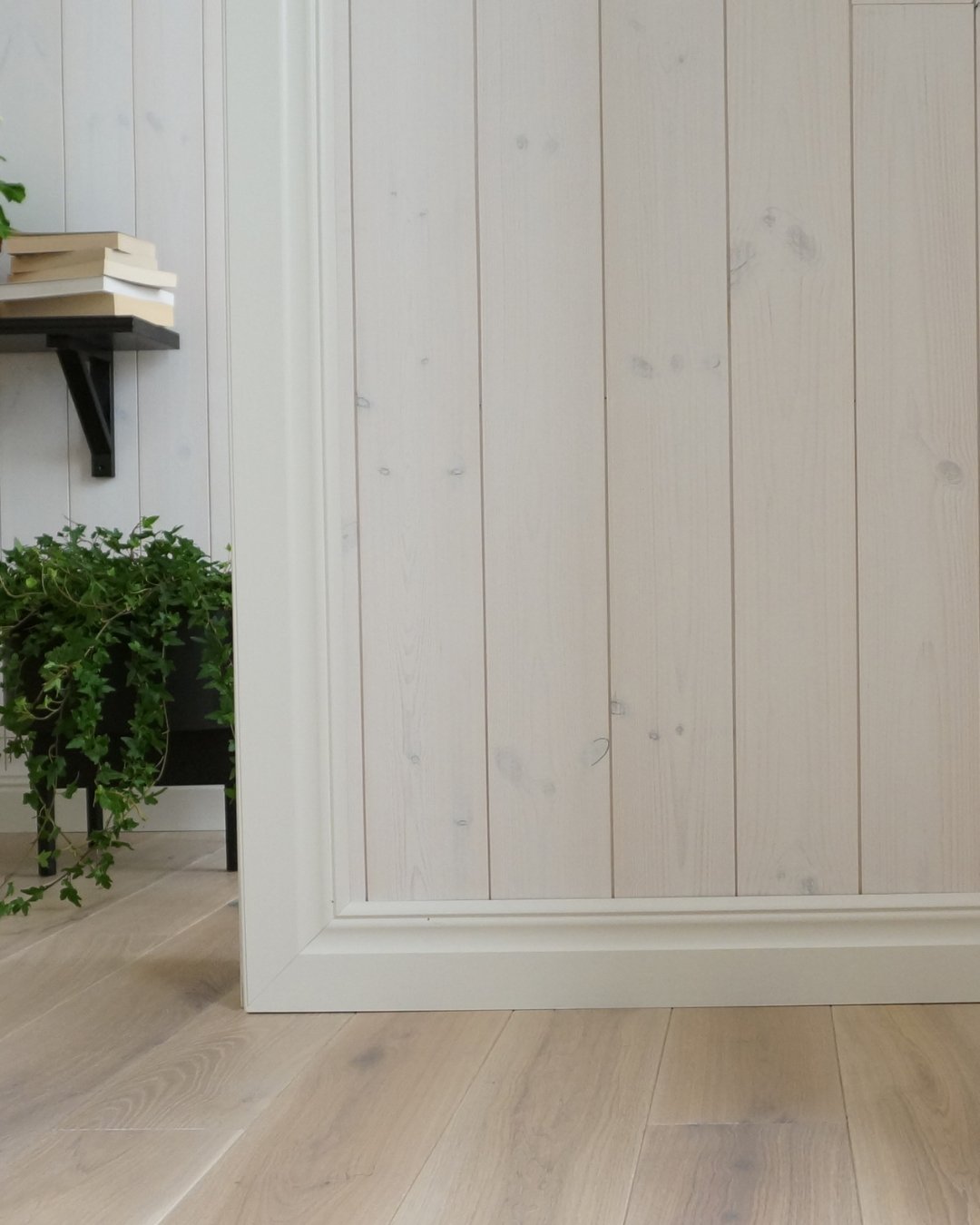 Vägg med vit panel och vita lister, samt trägolv