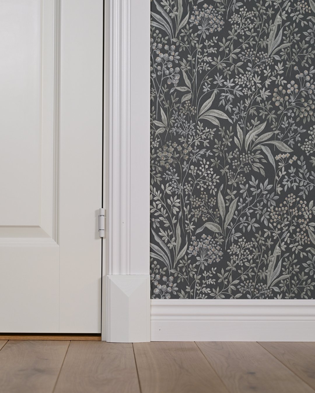 Vita lister och golvkloss, grön tapet med mönster, vit dörr och trägolv