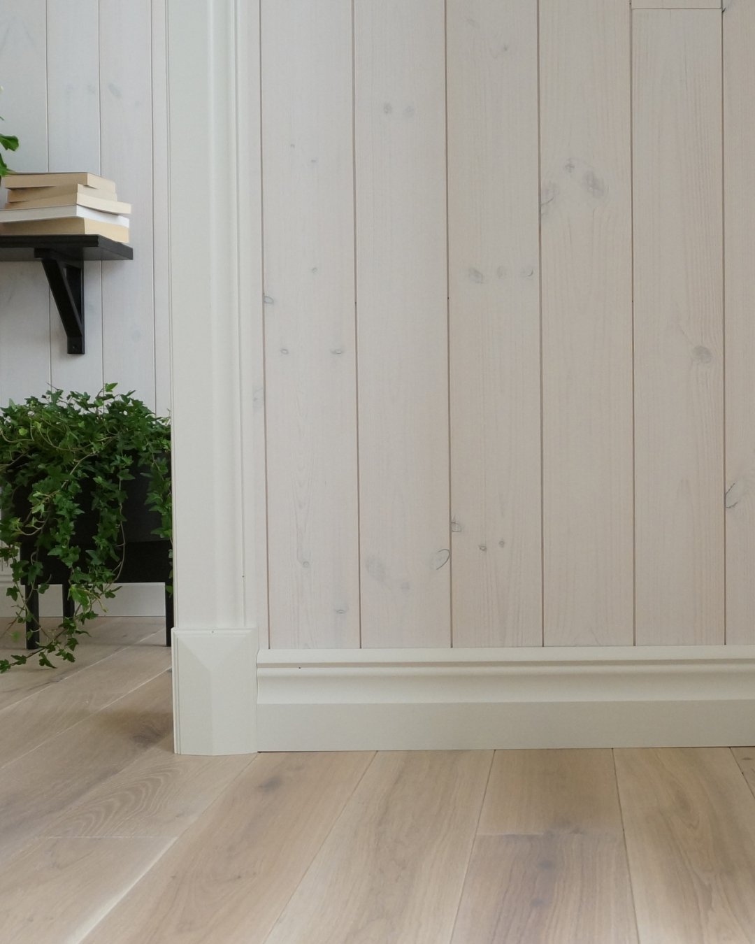 En vägg med vit panel, vita lister och trägolv