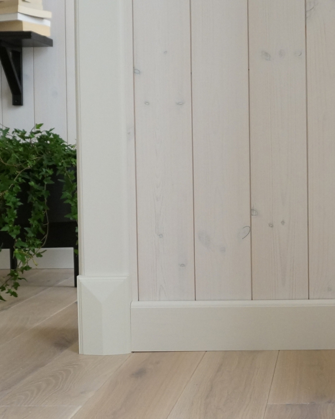 Vägg med vit panel och vita lister, samt trägolv