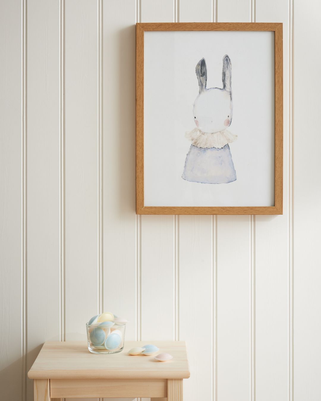 Vägg med vitmålad träpanel Trend Pärlspont, en träbänk och en tavla med brun ram