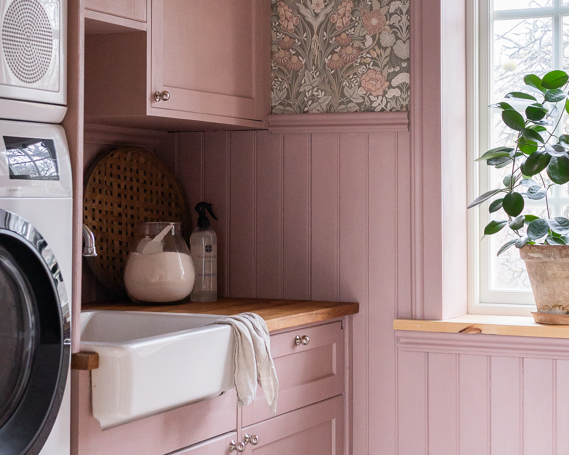 En tvättstuga med beige hylla och bänk med handfat, samt vit bröstpanel pärlspont