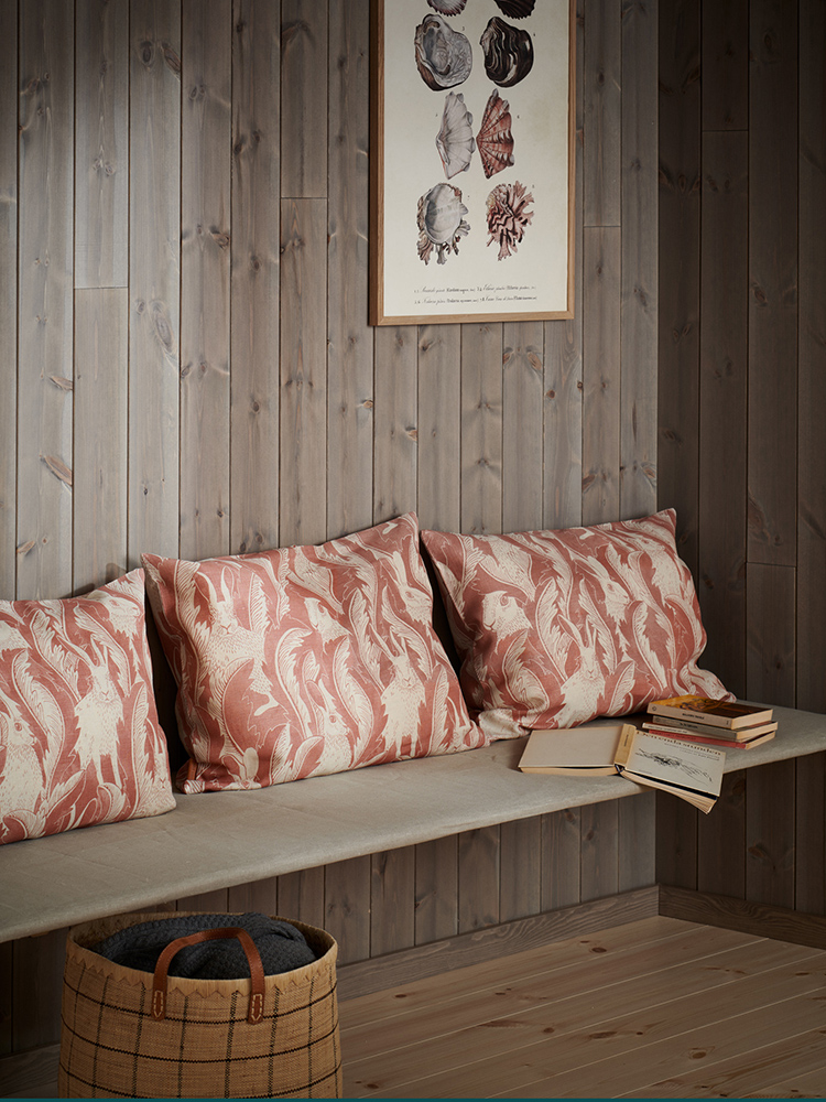 Träpanelen Stilla Gärdsgårdsgrå på väggen och färganpassad golvlist. Kuddar och böcker ligger på en platsbyggd bänk.