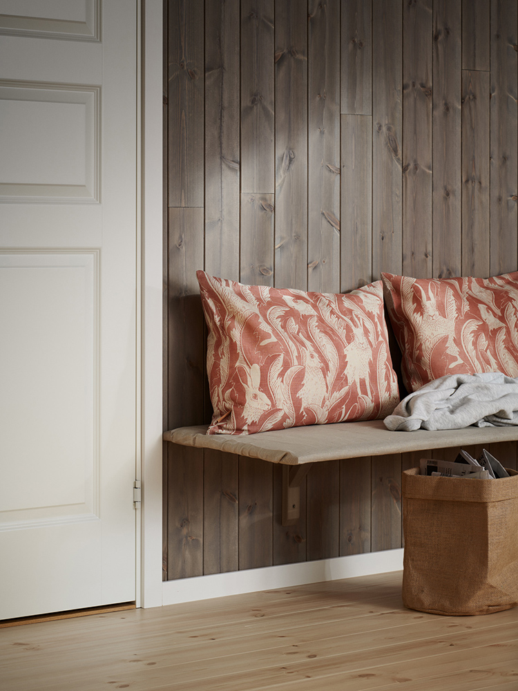 Träpanelen Stilla Gärdsgårdsgrå på väggen och vit golvlist och foder. Kuddar ligger på en platsbyggd bänk.