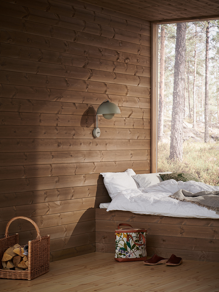 Träpanelen Stilla Skogsbrun sitter på väggarna och i taket. Rakt fram ett stort fönster med utsikt mot en tallskog.