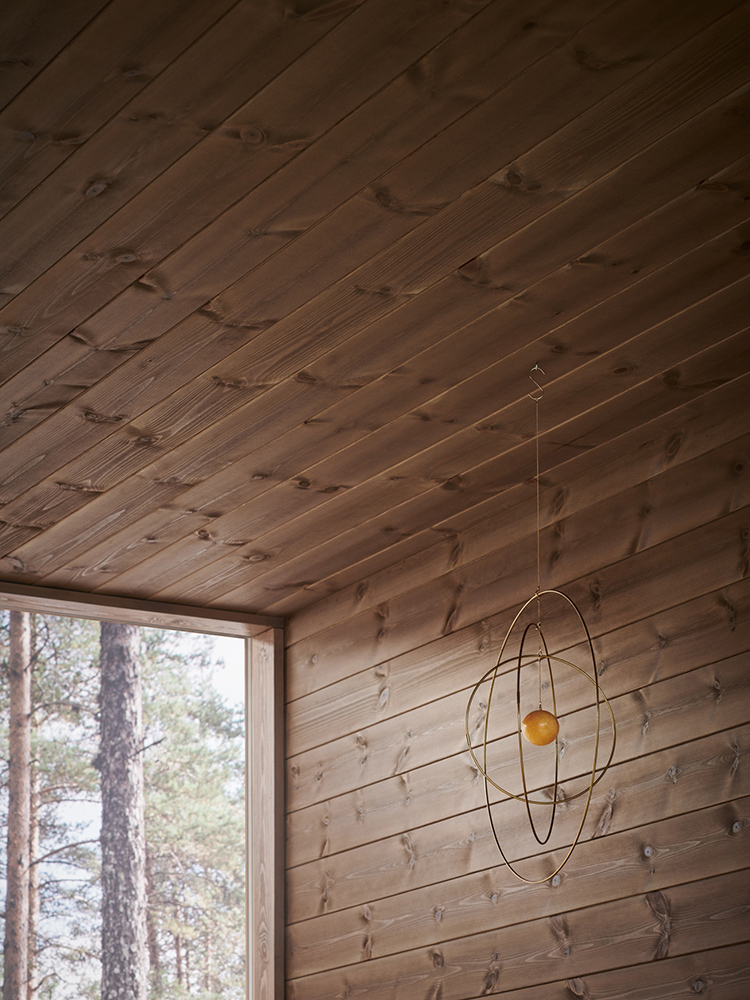 Träpanelen Stilla Skogsbrun sitter på väggarna och i taket. Rakt fram ett stort fönster med utsikt mot en tallskog.