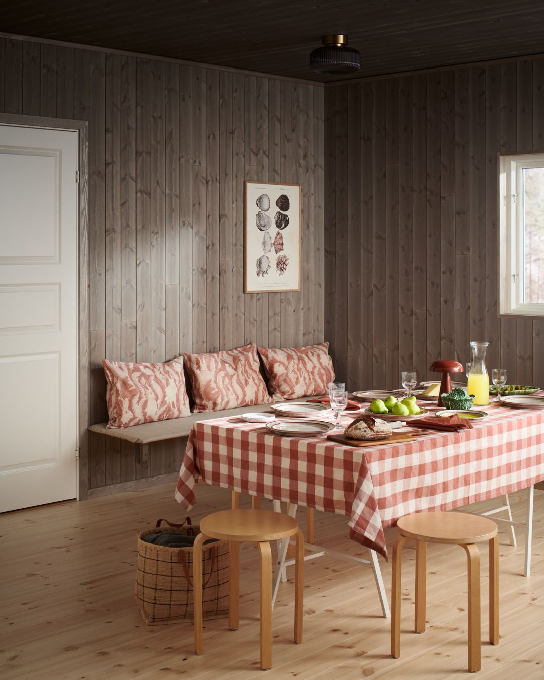 Matplats med träpanelen Stilla Gärdsgårdsgrå på väggar och tak samt dukat bord med rödvitrutig duk och fast sittbänk.