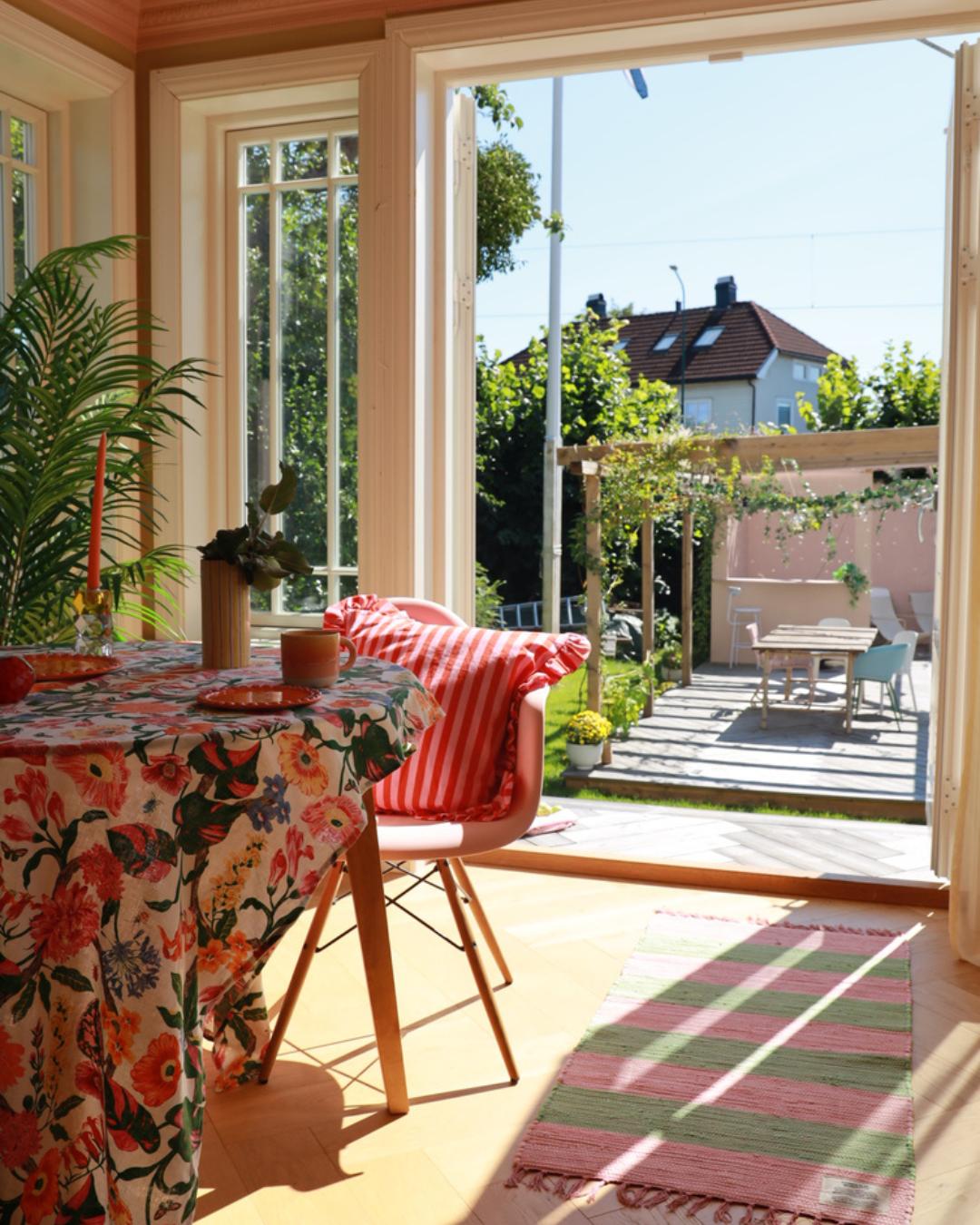 Innvendig spisestue med åpne franske dører ut til hage og terrasse. Utsikt til pergola og utebord i bakgrunnen, solrikt sommervær.