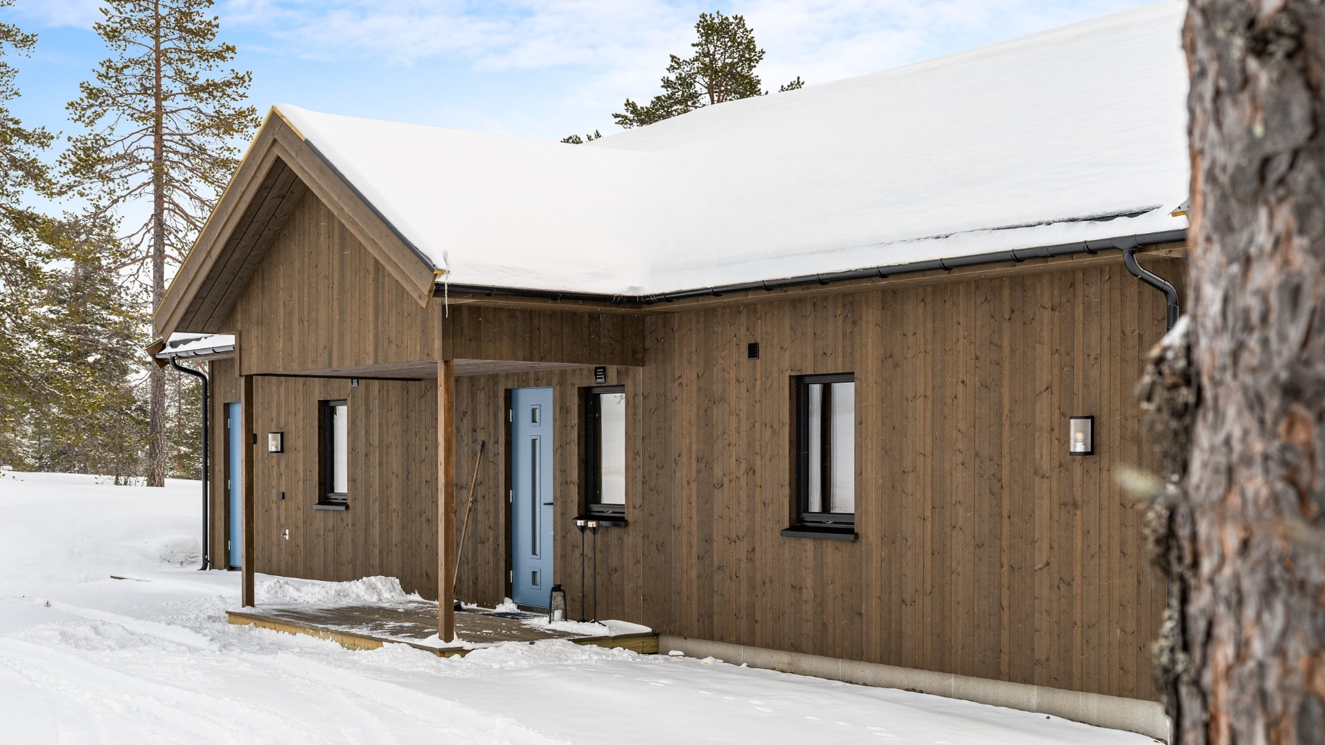 Inngangspartiet til en hytte med snø på taket