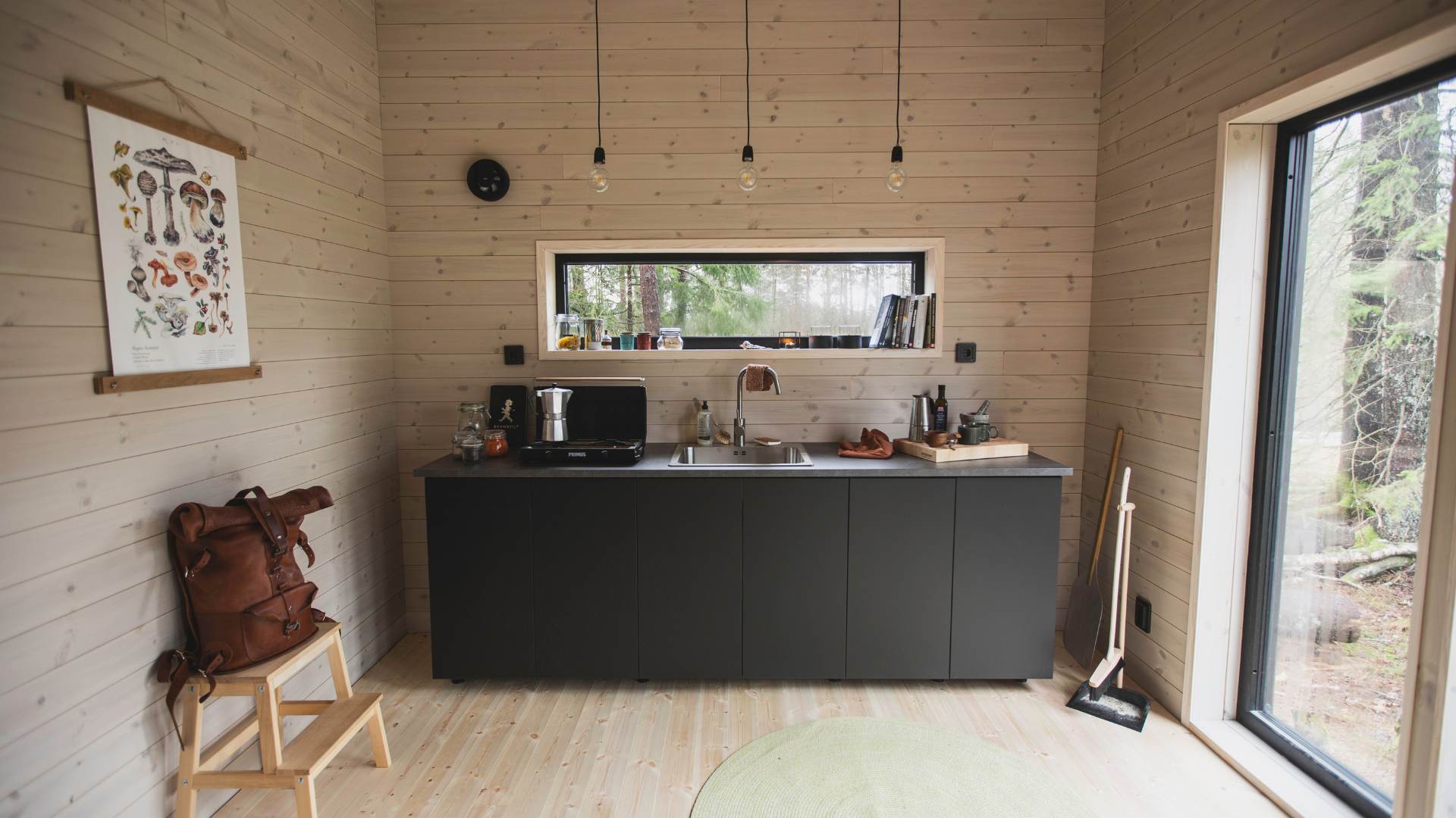 Storstuga med ljusa träpanelen Stilla Morgondis och ett svart kök och liggande fönster över
