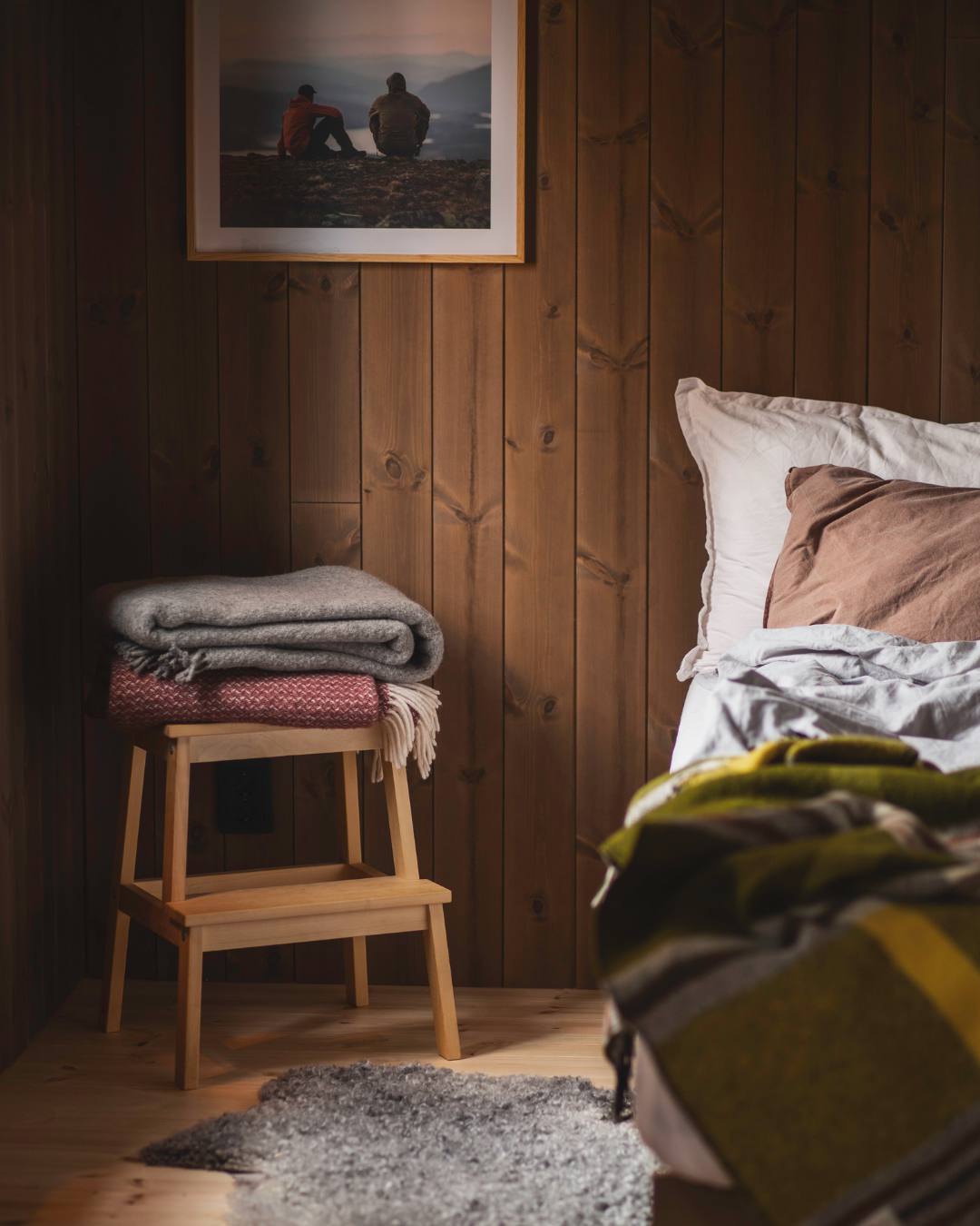 En säng och en pall i ett sovrum med bruna träpanelen Stilla Skogsbrun på väggarna