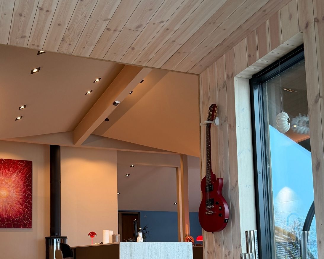 Lyst trepanel på vegg og i tak ved kjøkkenet på Haveng, med stor vindusflate og gitar på veggen.