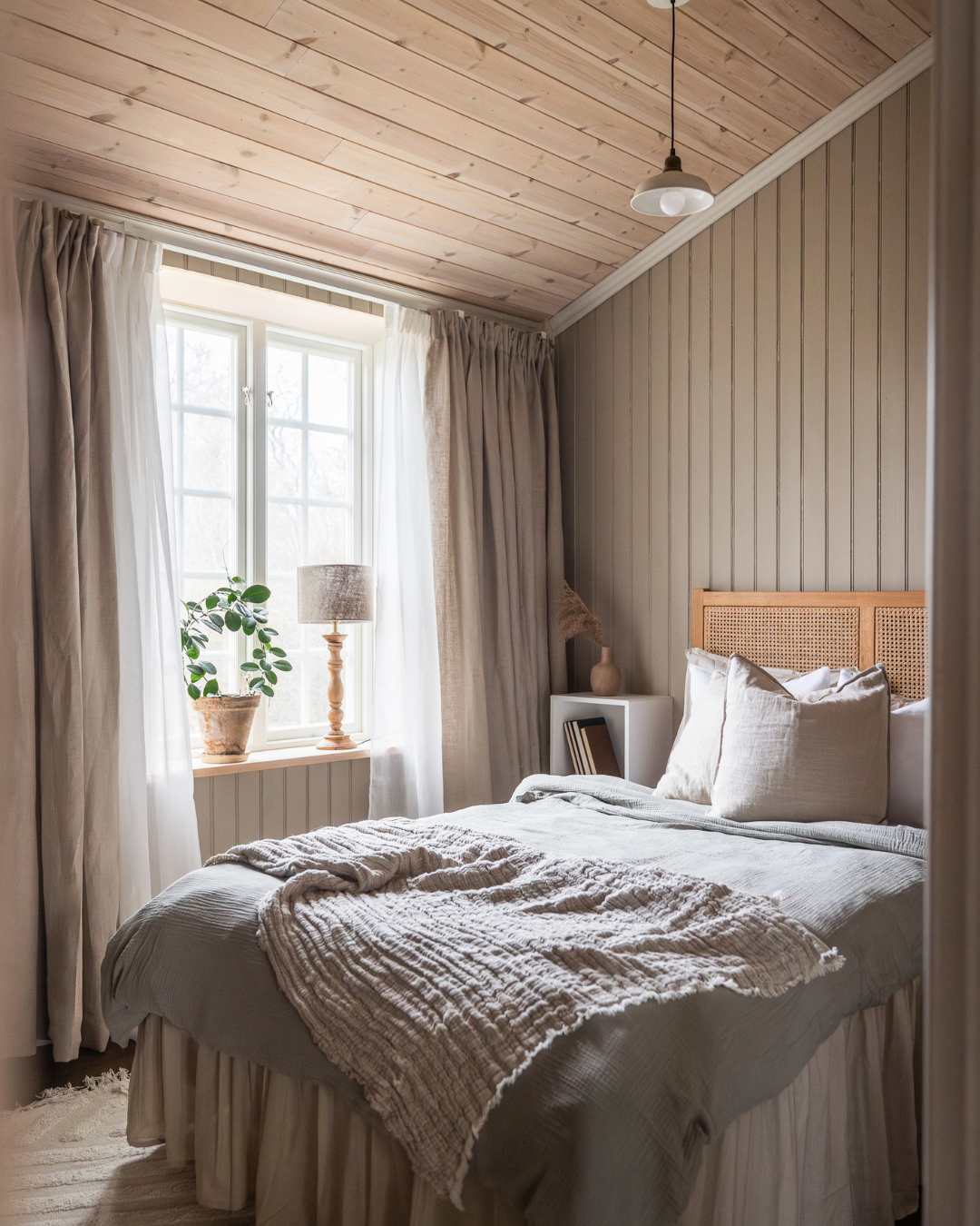 Soverom med stort vindu til venstre, bkomst og lampe i vinduskarmen. Lin gardiner. Dobbelseng med sengetøy av lin. Perlestaffpanel malt grønn på alle vegger.