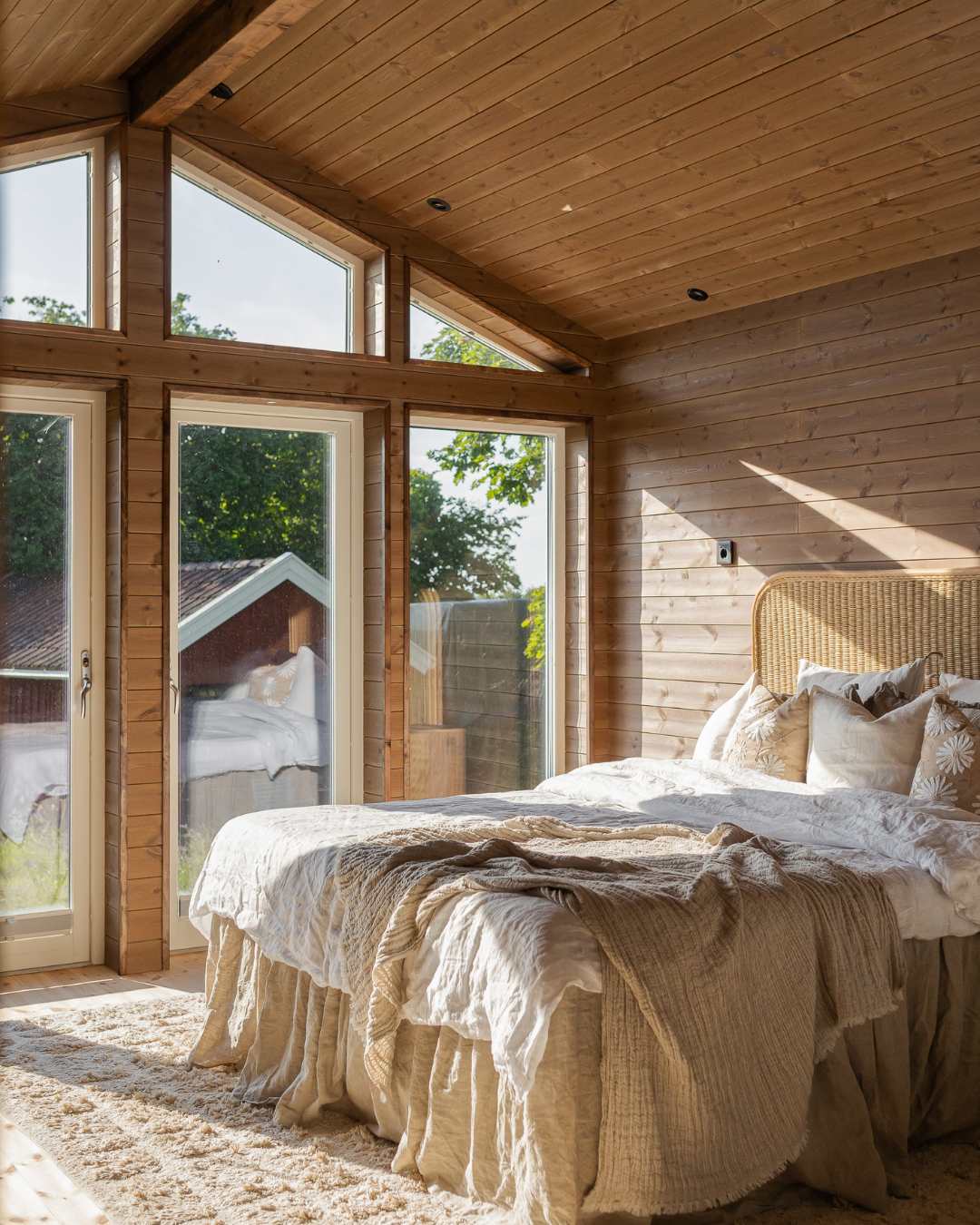 Sovrum med träpanel på väggar och tak samt höga fönster som släpper in dagsljus.