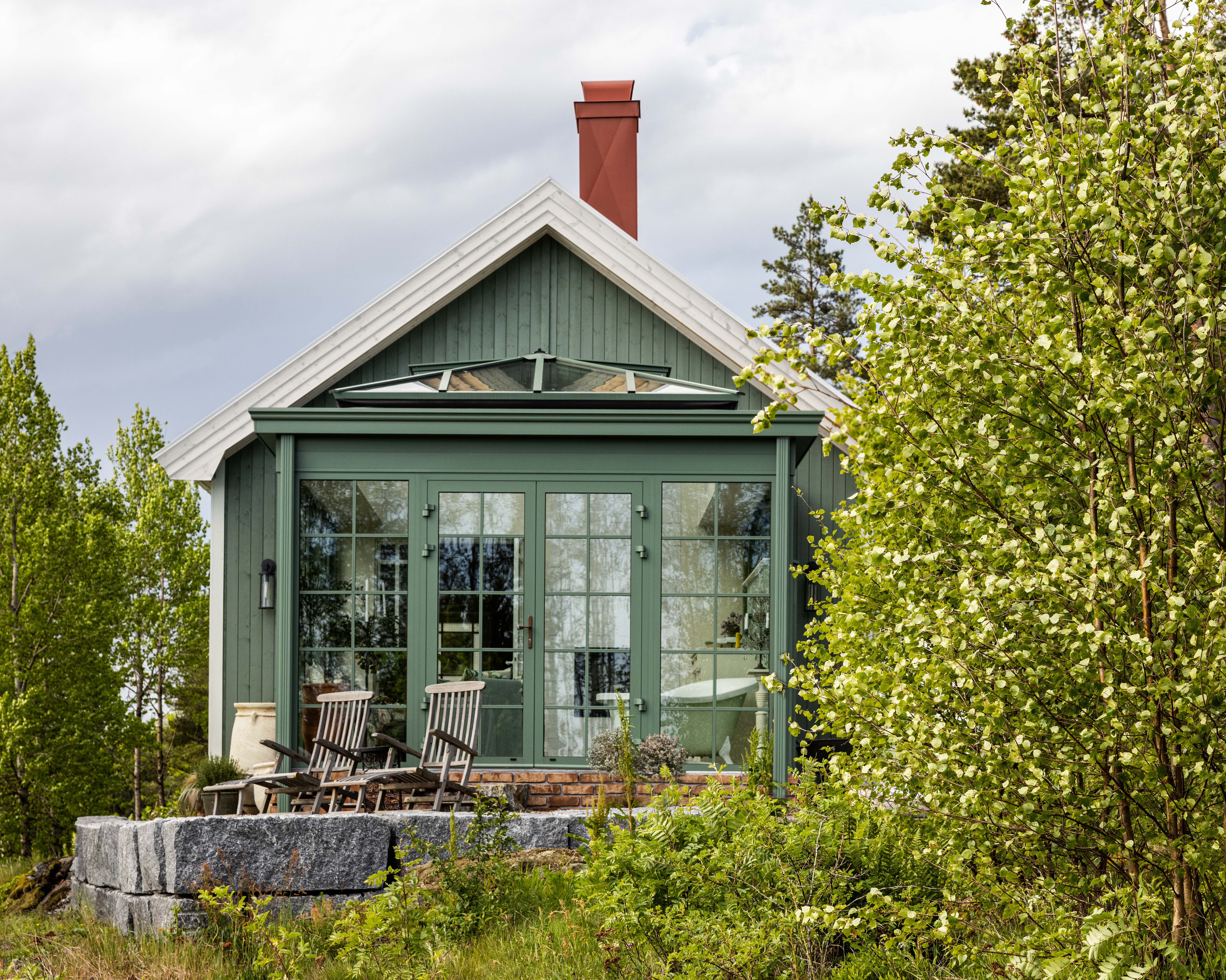 Lite hus med grønn kledning med orangerie i glass foran.