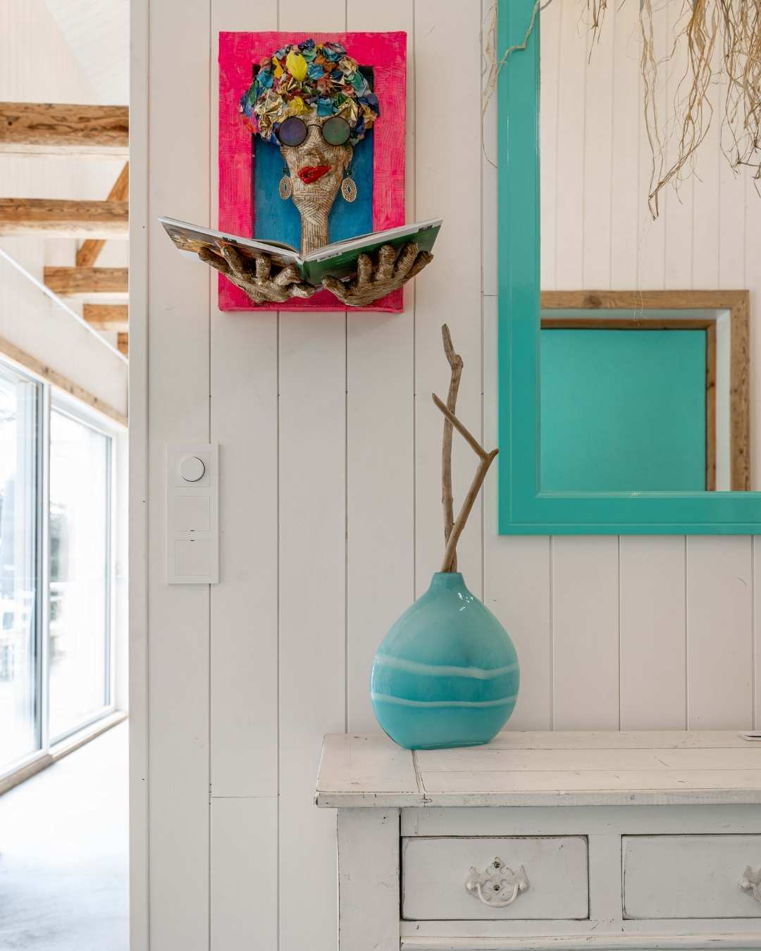 Stående innvendig hvitmalt panel med fargerik kunst og dekor i rødt og turkis.